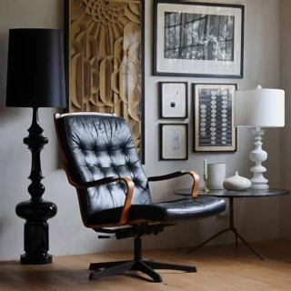 An image of a living room with art on the walls, a leather swivel chair, a table lamp and black floor lamp