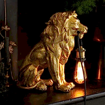 A gold lion lamp styled on a black surface with some accessories and some greenery.