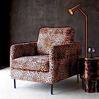 A leopard print armchair, with a floor lamp and a side table with glass on.