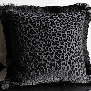 A pink fringed cushion with the words 'the show must go on', displayed on a neutral sofa.