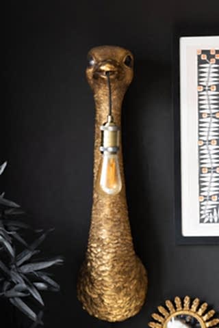 The Antique Bronze Ostrich Wall Light seen from the front, displayed on a dark wall and styled with a framed artwork, mirror and faux plant.