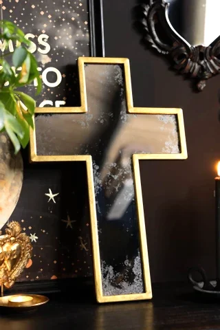 The Antique-style Gold Cross Wall Mirror shown against a black wall with quirky wall art.