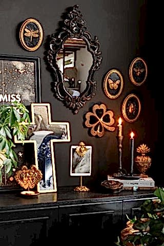 The Antique-style Gold Cross Wall Mirror shown leaned against a black wall in a gothic living room scene with black and gold wall art and accessories.