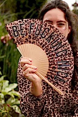 The Be Fucking Nice Leopard Print Fan being held by a model outdoors.