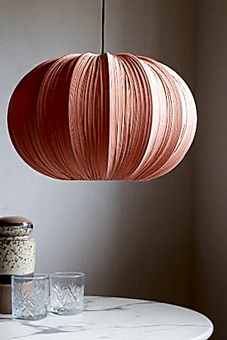 The Blush Pleated Fabric Ceiling Light hanging in front of a neutral wall above a marble table, styled with some glasses and a storage jar.
