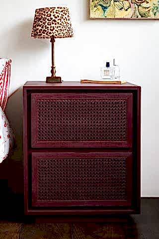 The Burgundy Rattan Bedside Table styled next to t bed with a lamp and some accessories on.