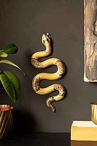The Ceramic Snake Wall Art displayes on a wall next to a potted plant, a book, a canvas and another small plant pot.