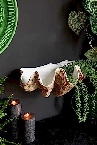 The Clam Shell Wall Shelf displayed on a black wall, styled with lit candles, plants and green home accessories.