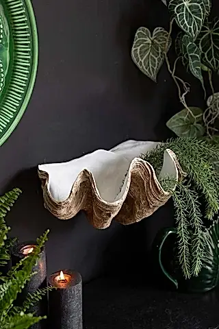 The Clam Shell Wall Shelf displayed on a black wall, styled with lit candles, plants and green home accessories.