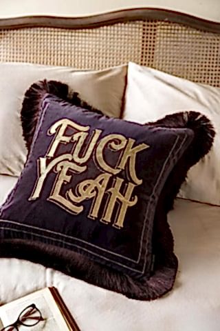 Decorative pillow with 'FUCK YEAH' text on a bed.