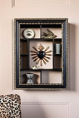 The Ornate Black & Gold Framed Wall Shelf styled with various accessories, displayed on a wall above a leopard print sofa.