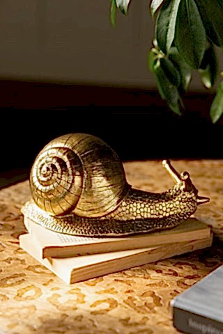 The Gold Snail Ornament styled on a stack of books on a wooden table.