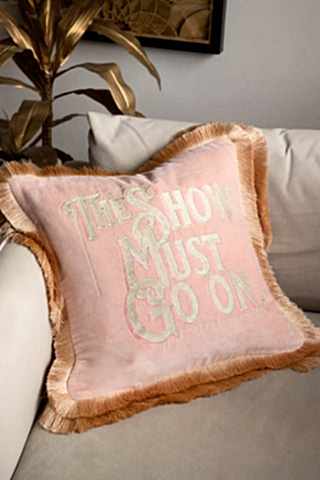 The Pink Velvet Double-Fringed Show Must Go On Embroidered Cushion displayed on a white armchair.