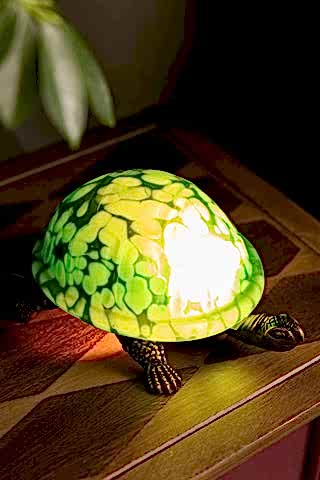 The Green Speckled Glass Turtle Table Lamp shown wit the light on.
