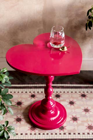The Hot Pink Heart Metal Side Table shown styled on a pink tiled runner against plaster walls. 