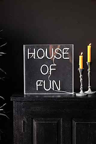 The House Of Fun Neon Light Box switched off and styled on a black unit next to two lit candles.