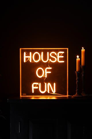 The House Of Fun Neon Light Box illuminated and styled on a surface next to two lit candles.