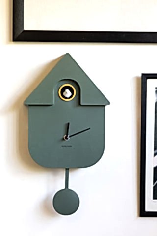 A green cuckoo clock with a pendulum and bright white cuckoo. The clock is hung on the wall.