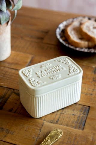 The L'Amour Toujours Butter Dish shown on a wooden kitchen table with toast in the background.