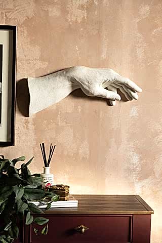 The Large White Helping Hand Wall Art shown on a plaster wall above a burgundy and wood console table. 