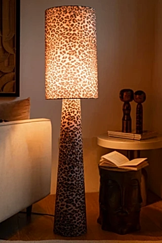 The Leopard Love Print Floor Lamp switched on and displayed next to a sofa and side table with various accessories.