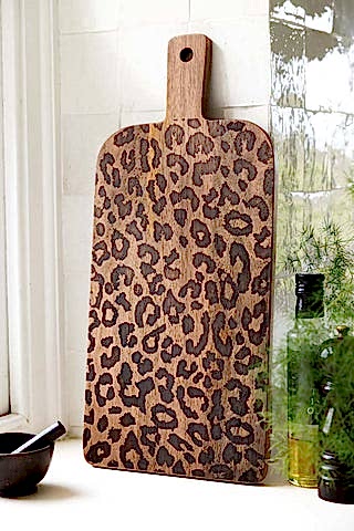 The Leopard Print Tall Wooden Serving Board shown in a kitchen against white zellige tiles. 