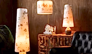Three printed lights displayed on/around a sideboard, chair and plant, in front of a dark wall.