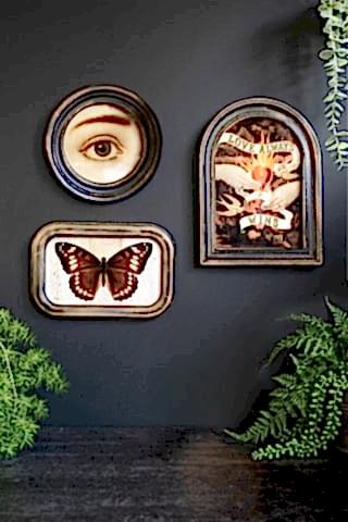The Vintage-Style Love Wins Framed Wall Art styled on the wall along with two other artworks, surrounded by plants.