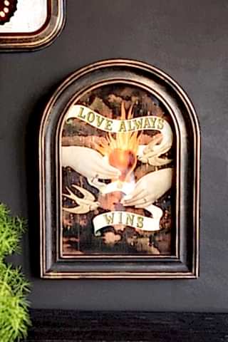 The Vintage-Style Love Wins Framed Wall Art displayed on a dark wall next to another artwork and a plant.