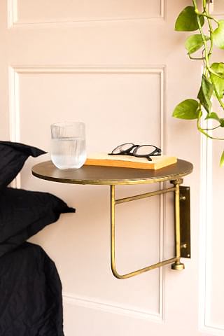 The Metal Table & Wall Shelf styled next to a bed, with a water glass, book and some glasses on, next to a plant.