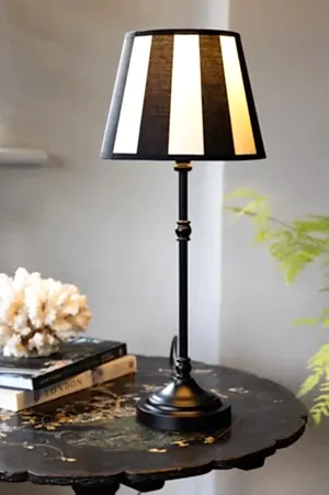The Monochrome Bistro Table Lamp switched on and styled on a table with some accessories.