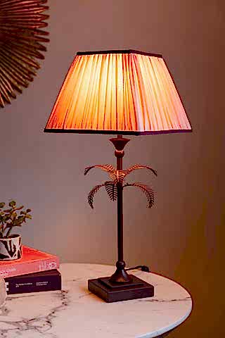 Styled image of the Palm Tree Table Lamp - Pink & Burgundy, switched on and on a white marble table