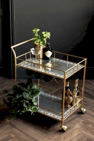 The Party People Only Gold Drinks Trolley, decorated with plants and drinks bottles on a dark background. 