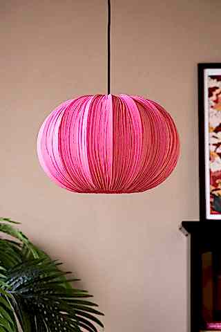 The Hot Pink Pleated Fabric Ceiling Light hanging with a plant, fireplace and art print in the background.