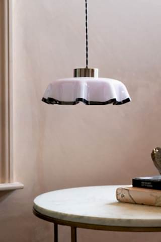 The Pink Pleated Glass Easyfit Ceiling Light Shade shown against plastic pink walls, hanging over a coffee table. 