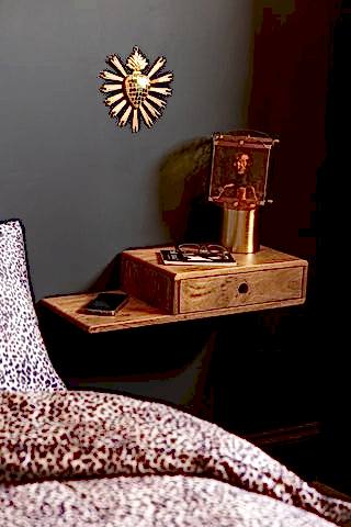 Secret Nook Wall Shelf With Drawer shown styled as a bedside table against a black wall with an amber table lamp.