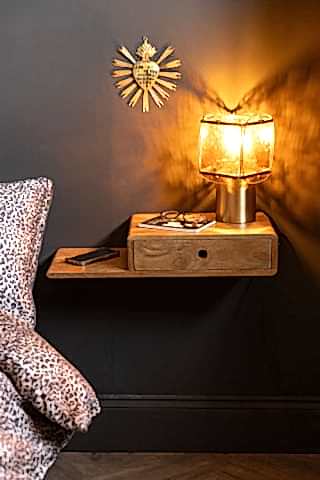 The Secret Nook Wall Shelf With Drawer shown straight on next to a bed with leopard bedding and a black wall.