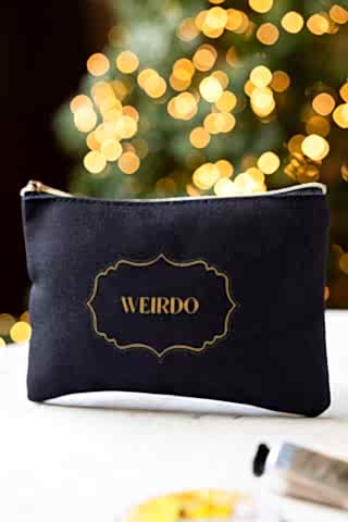 The Weirdo Black Canvas Pouch shown on a marble table with fairy lights in the background.