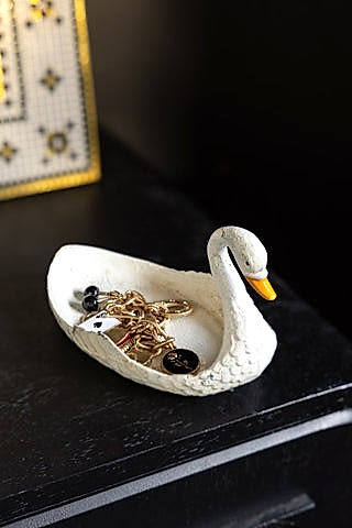 The White Swan Cast Iron Trinket Dish shown holding jewellery on a black wood console.