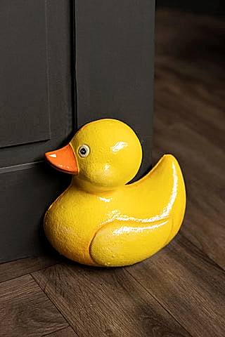 The Yellow Duck Cast Iron Doorstop in front of a black door.