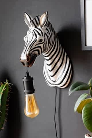 The Zebra Wall Light displayed on a black wall next to some plants and a framed artwork.