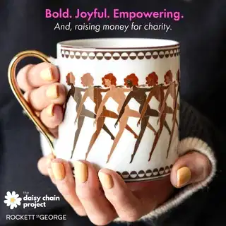 Mug with dancing women design held by a hand, with text about charity and the Daisy Chain Project.