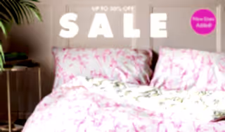 A bed with palm print bedding on, with the  words 'up to 50% off sale, new lines added!' above.