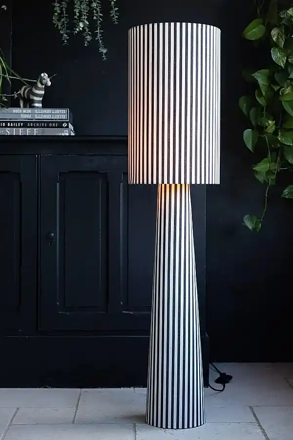 Lifestyle image of the Black & White Stripe Floor Lamp on with a black cabinet